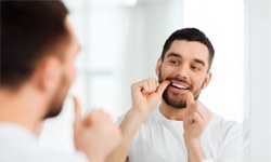 man flossing teeth in bathroom mirror 