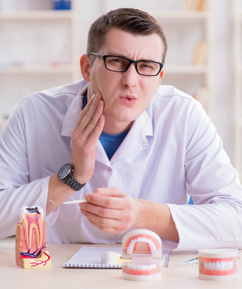 Dentist putting his hand to his cheek while slightly grimacing.
