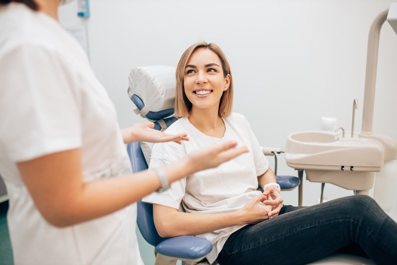 Woman smiling in dental chair as dentist explains something to her